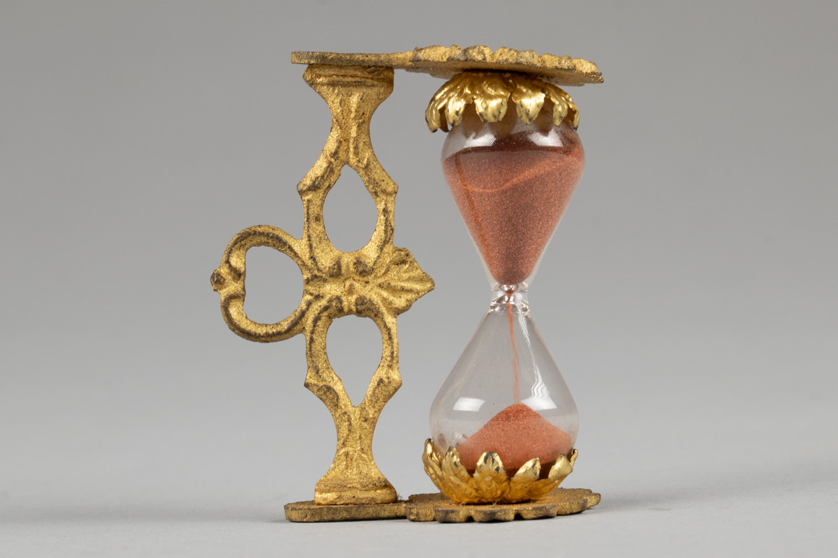 Timeglass med stativ av gullforgylt metall. Tiden det tar for at sanden skal renne fra den ene kolben til den andre er ca 2,32 min.