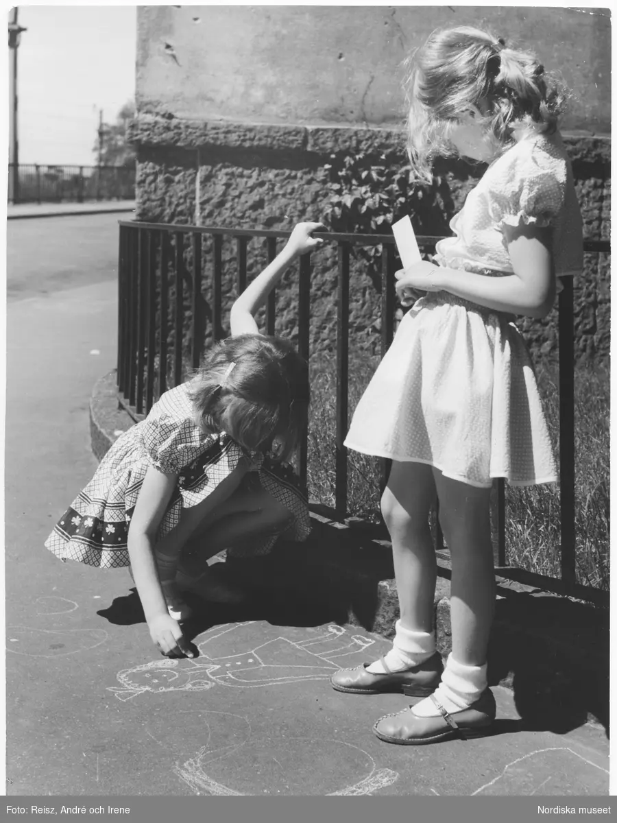 Två flickor leker och ritar på gatan under sommarlovet i Sverige.