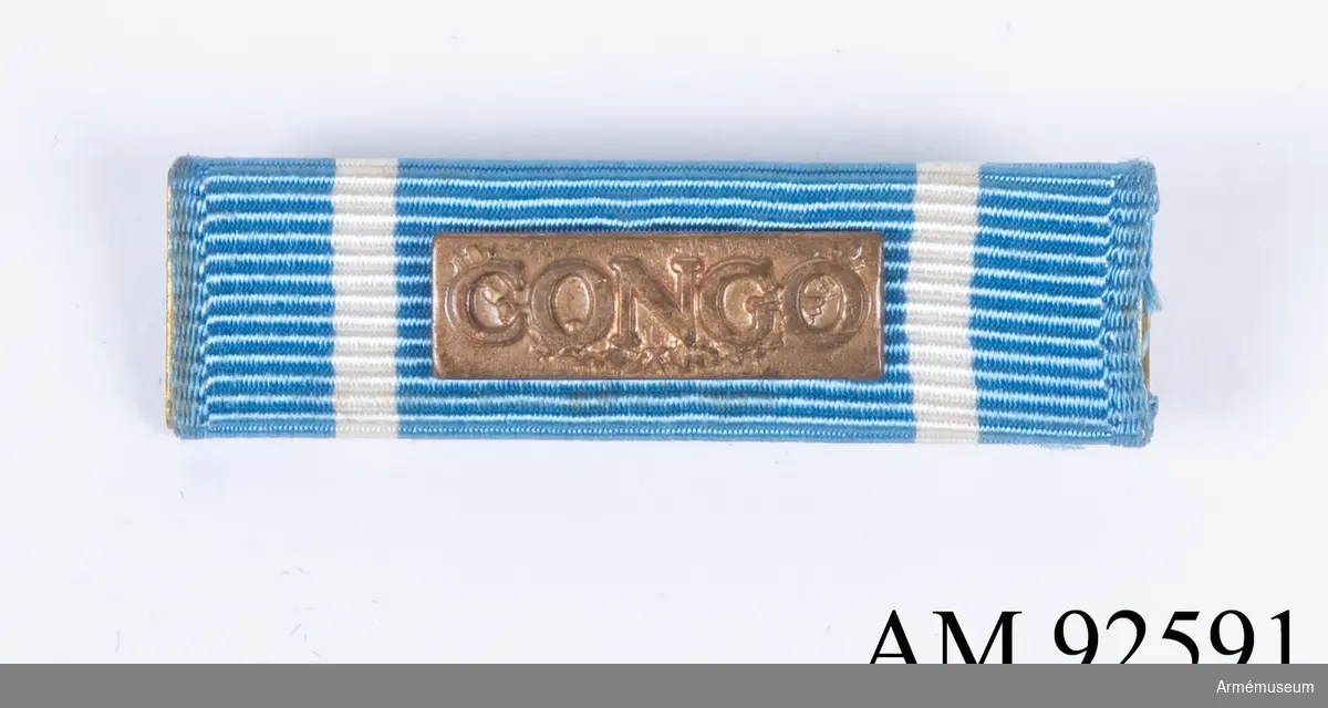 Släpspänne till FN-medalj i blått band med vit rand i kanten. På framsidan sitter ett litet bronsmärke med texen "Congo". En enkel säkerhetsnål är löst fastsydd på baksidan av bandet.
Band i blått och vitt användes när insatsen i Kongo inledds 1960. 1962 byttes banden till färgerna blå-vit-grön som på medaljen som spännet hör till.