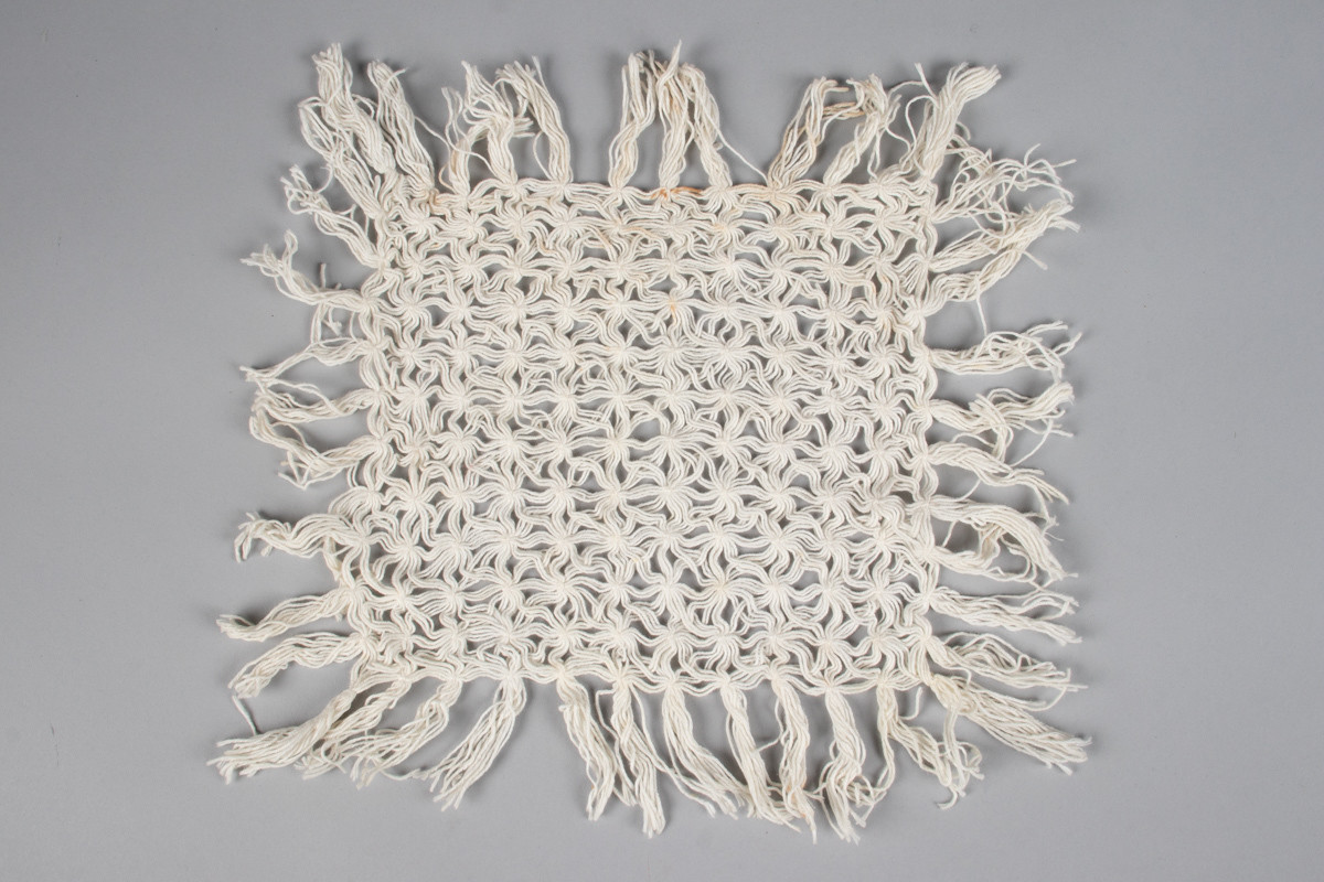 Rektangulær duk med knutemønster og frynser. Laget av bomullstråd. Knytteteknikk