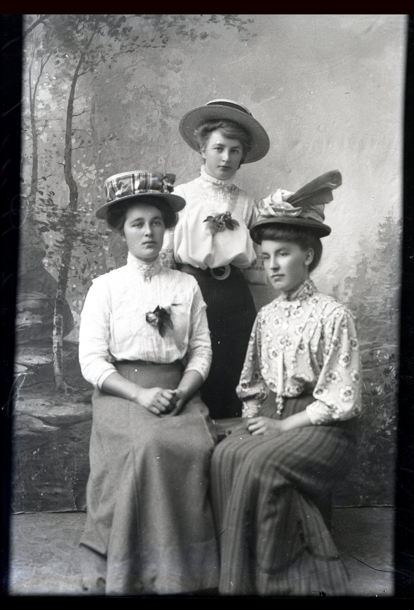 Atelierfoto. Helfigurer. Tre kvinner med hatter, to siter og den tredje står bak.
Skrevet på negativet: Lisbet Rustad, se bilde GM_MG.00898_1.