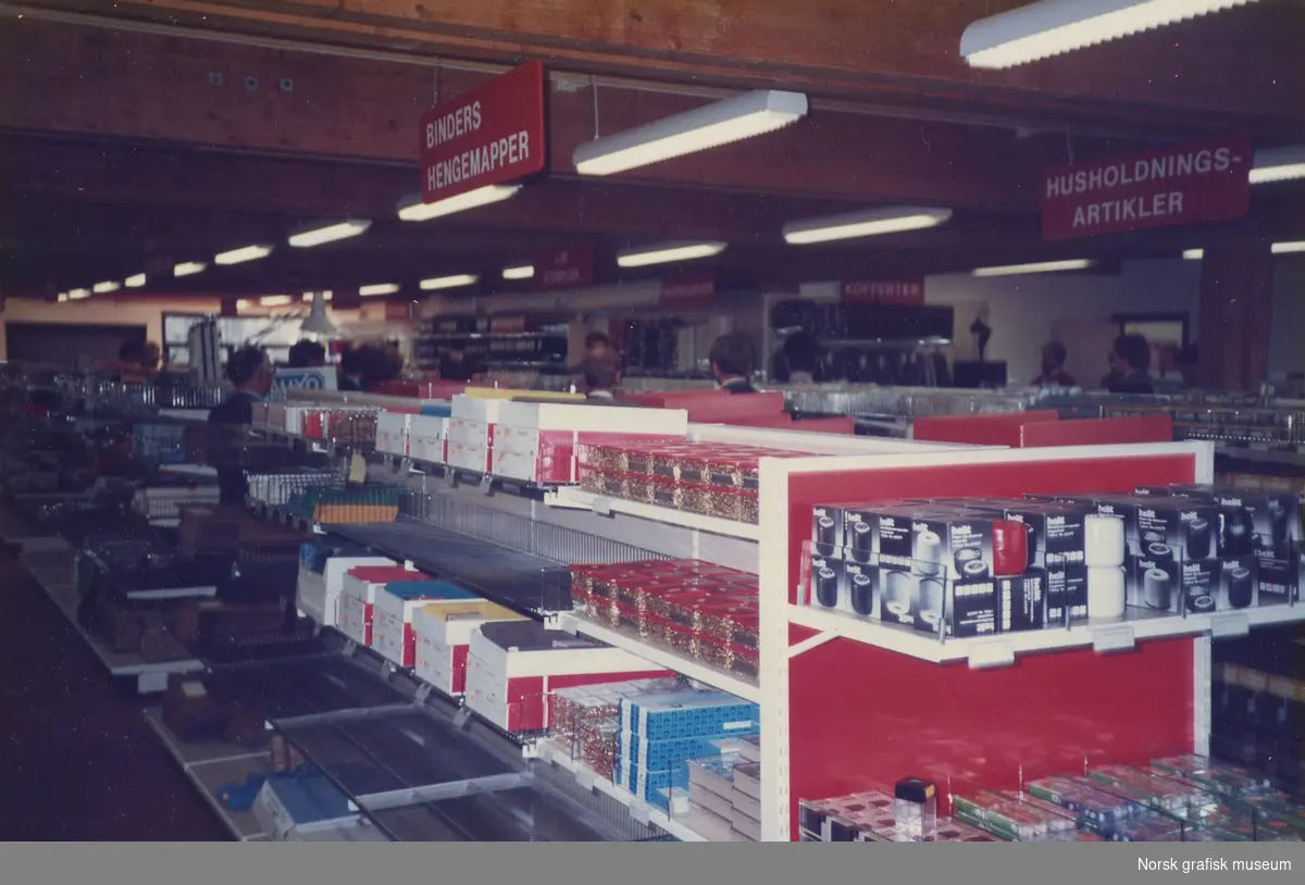 Interiørfoto som viser røde og hvite hyller fylt med produkter. I taket henger lysarmaturer.
