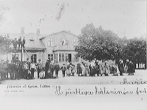 Vykort, "Folkskolan vid kyrkan, Tvååker" med barn och personal på skolgården. Tidigt 1900-tal.