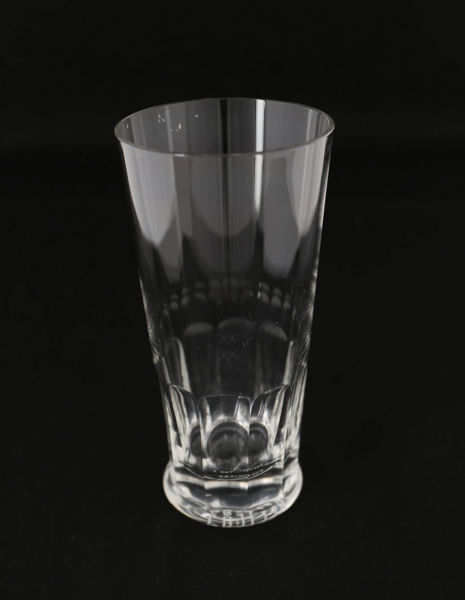 Blåst ølglass av glass med høy, konisk form og fasettslipt dekor nederst ved rund, flat fot.
