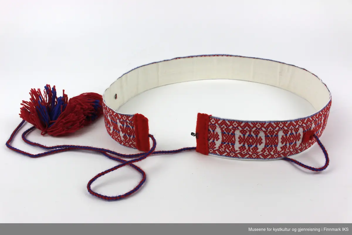 Et samisk belte vevd av ull og bomull. Belte har flettet bånd med dusker, og beltespenne slika at belte kan reguleres i lengde. På innsiden av belte er det påsydd lerret som gir belte en avstivet form.    

Belte er dekorert med et geometrisk mønster i rødt og blått. Mønsteret brukes i Karasjok, Porsanger, Utsjok og Tana dalen.
