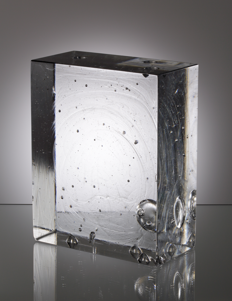 Formgivet av Sven Palmqvist. Glasblock. Rätblocksformad, i ofärgad glasmassa, med ingjutna luftbubblor. Två väggar med slipade kulor. Ingick som en del av glasvägg.
