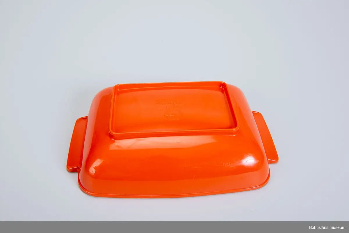 Rektangulärt serveringsfat eller uppläggningsfat med rundade kanter med dekorerade handtag i orange melaminplast.