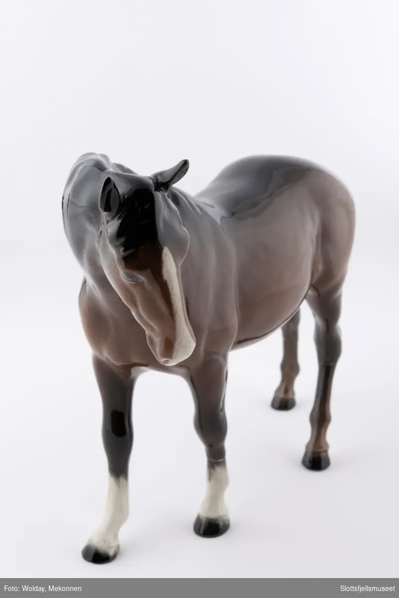 Stående hestefigur i porselen, hodet litt til siden. Kalles Beswick Bois Roussel racehorse. Brun glassert hest med lys mule.
Stemplet med Beswick merket under på magen.