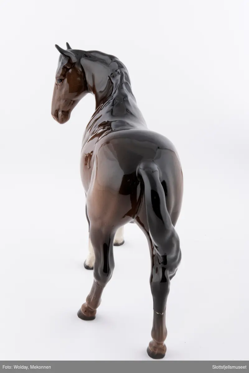Stående hestefigur i porselen, hodet litt til siden. Kalles Beswick Bois Roussel racehorse. Brun glassert hest med lys mule.
Stemplet med Beswick merket under på magen.