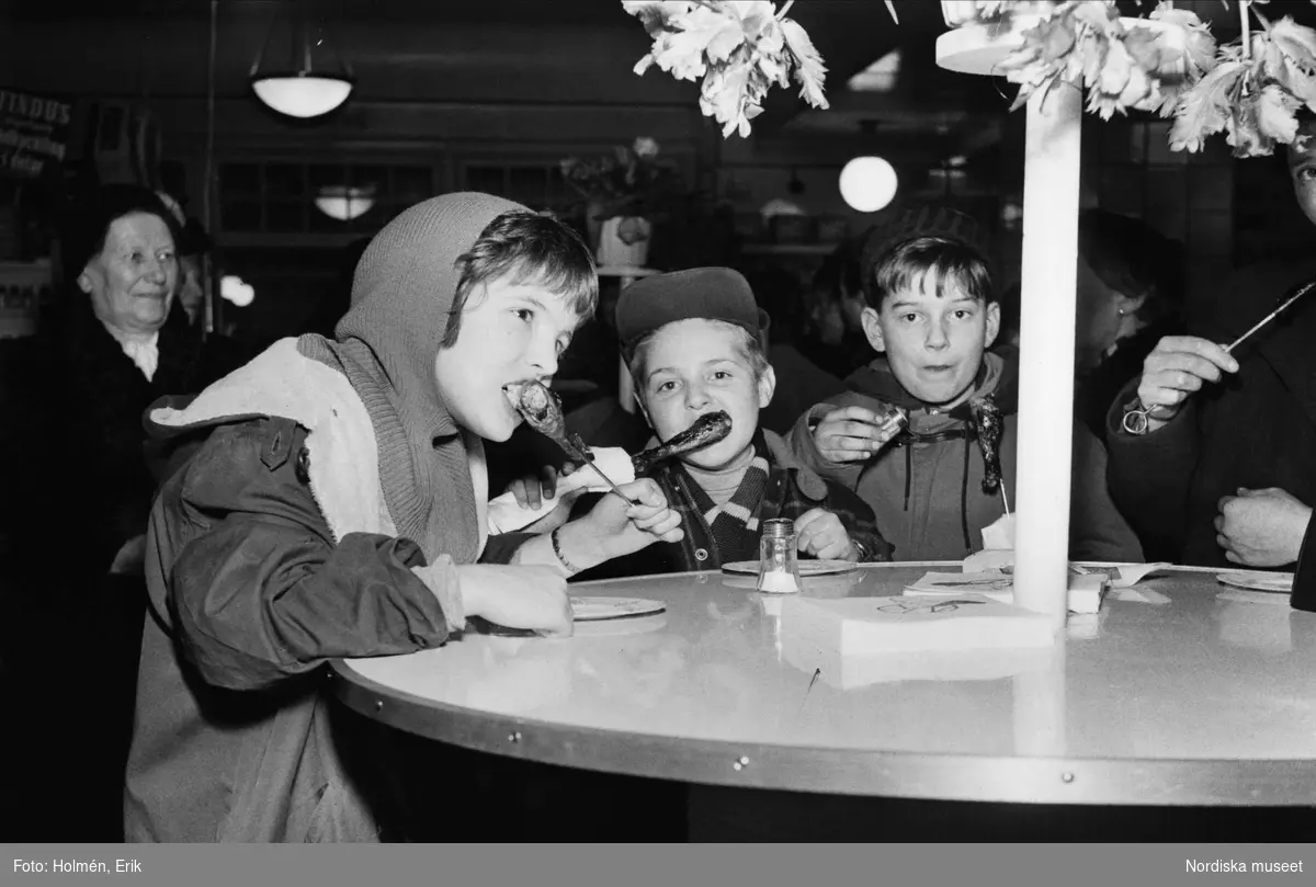 Barn som äter kycklingklubbor. Demonstration av Grillman, den elektriska bordsgrillen och Findus gödkyckling på varuhuset Nordiska Kompaniet 1956.