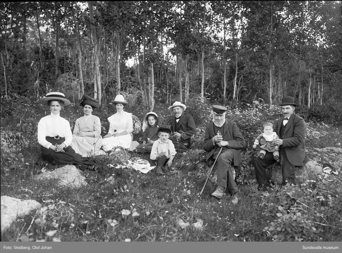 Gruppbild från en utflykt med fikakorg i en skogsglänta, tre kvinnor, tre män och tre barn.