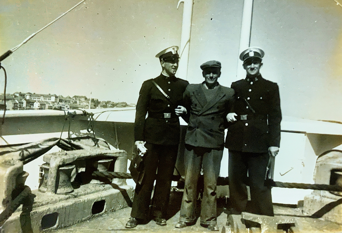To uniformerte politikonstabler står på et båtdekk med en sivilkledt mann mellom seg.