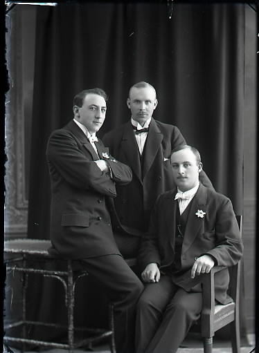 Ateljébild. Tre män i halvfigur. Två bär blommor på kavajslagen. Beställare och sannolikt avbildad: Robert Eriksson, Valskvarnen Falkenberg. (Se även bildnr GB2_5918)