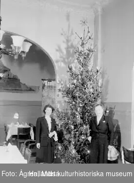 Julbord med garnerat grishuvud på källaren Munken i Stadshotellet, Varberg. Bild 2 visar ett par kvinnor ur personalen vid matsalens julgran.