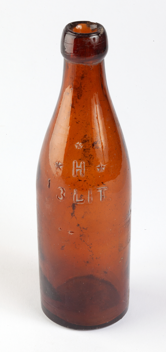 Ölflaska i brunt glas. Märke: H omgivet av 3 stjärnor med texten 1/3 LIT. under. I botten årtalet 1912.