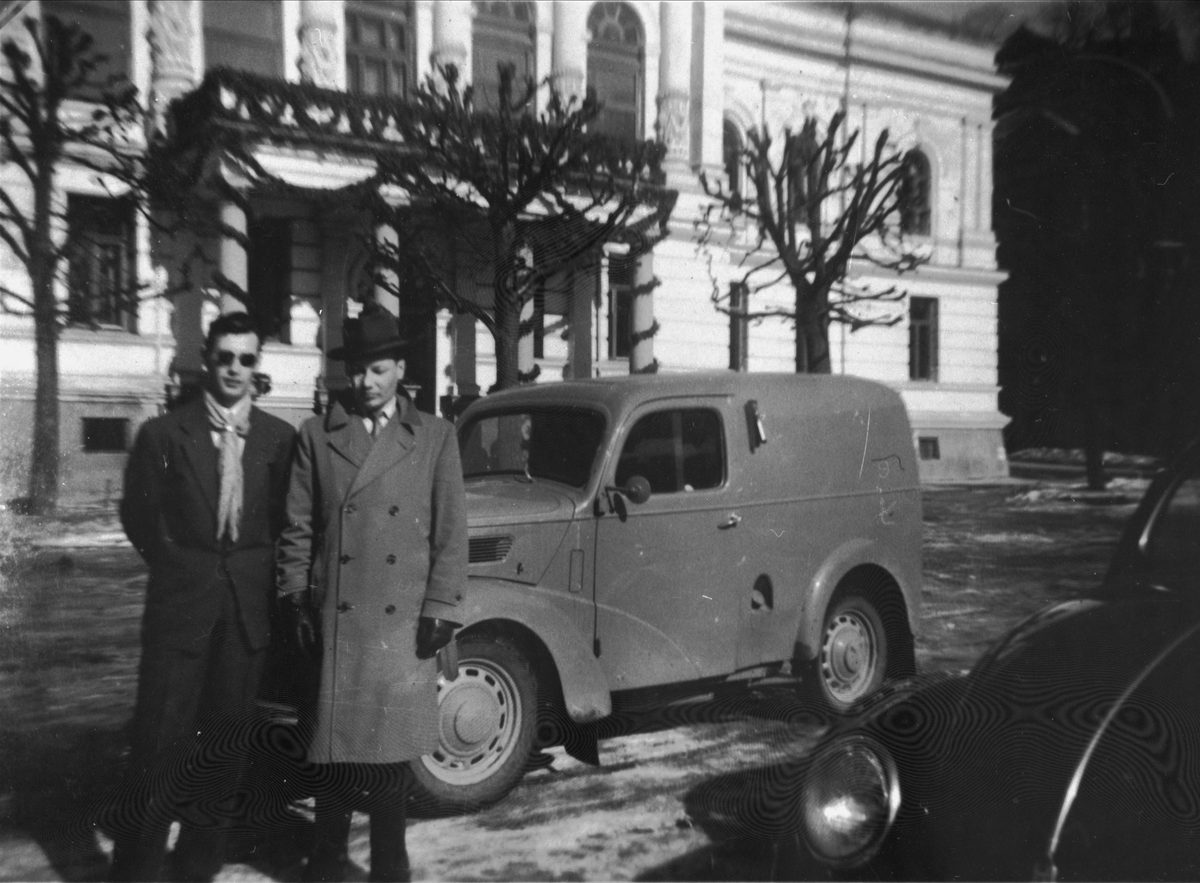 To menn stående ved en bil foran rådhuset i Skien.