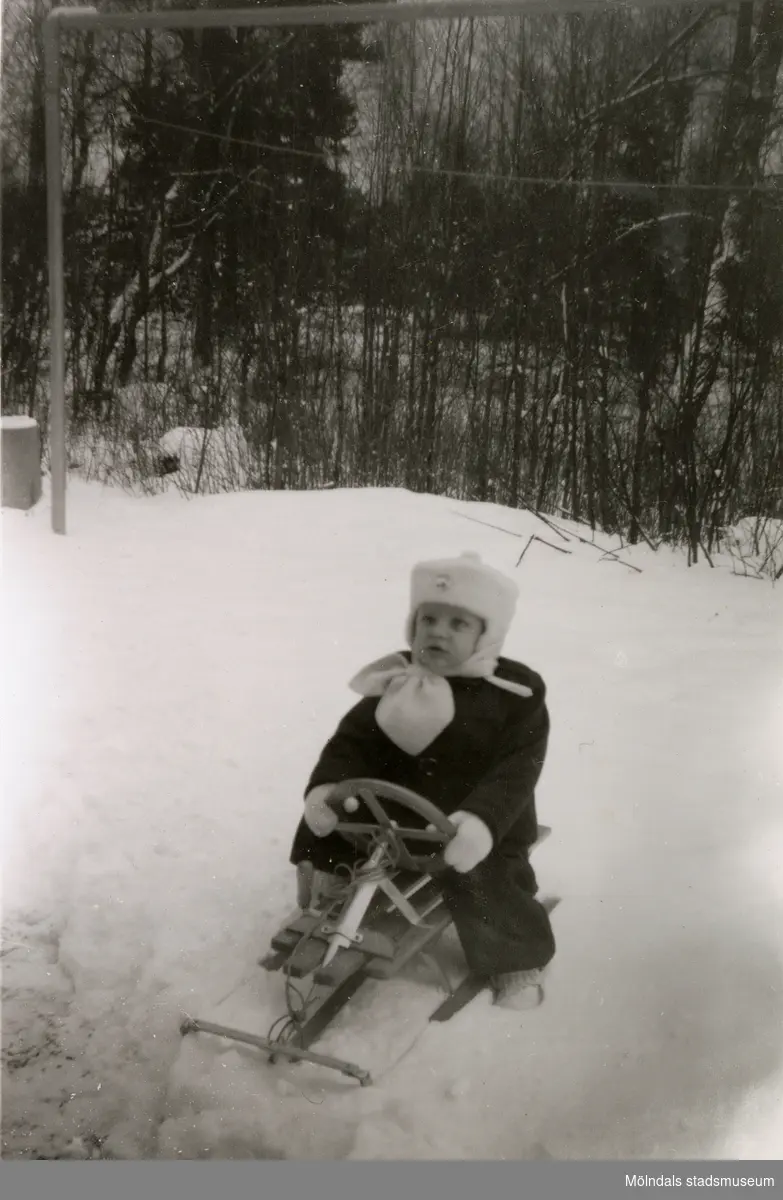 Vinter i Lackarebäck, Mölndal, på 1950-talet. Jan Erik Wäne sitter på sin kälke i snön.