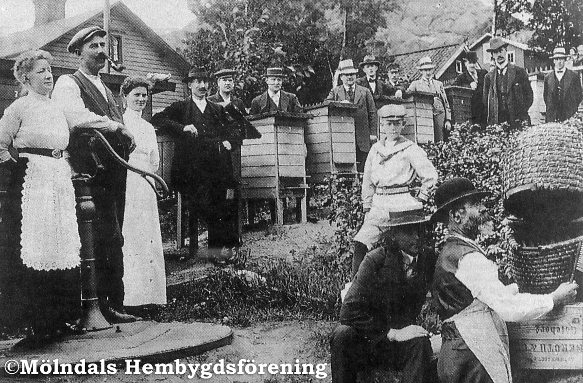 Mölndals biodlarförenings första instruktionskurs. Fotografi taget vid Gunnebogatan i Lackarebäck, östra Mölndal, år 1914. Till vänster, på brunnskaret, ses Eric Hedenberg tillsammans med sin fru. Det är i deras trädgård föreningens medlemmar är samlade. AF 9:27.