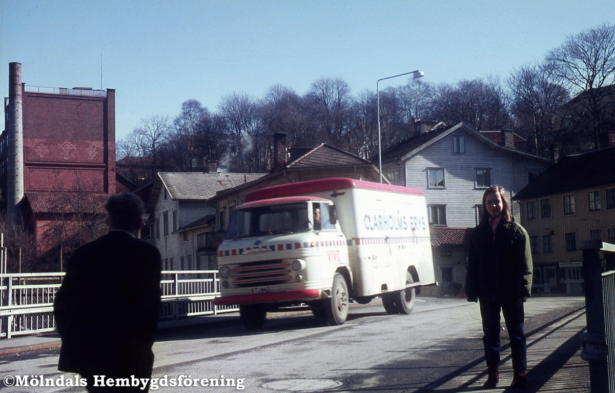 En lastbil och två fotgängare på Forsebron i Mölndal, 1970-tal. I bakgrunden till vänster ses Stora Götafors, i mitten Götaforsliden 1-5 och till höger Götaforsliden 6 (Roten M1) och 4 (Roten M2).