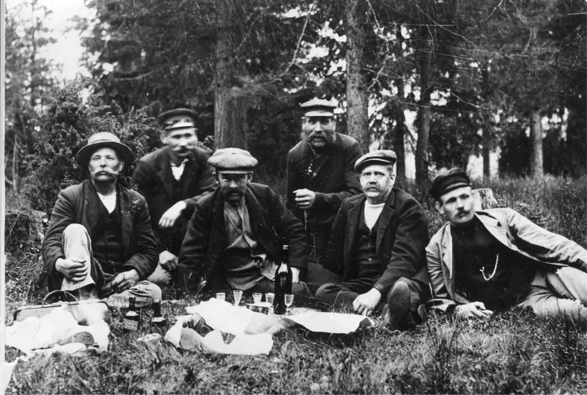 Bildens rubrik är "En hutt i skogsbacken". På bilden syns i vänstra kanten August Lindersson, karl var vedhandlare och bodde vid Dammtorp i Turinge. Näst längst till höger ser vi Carl Blom