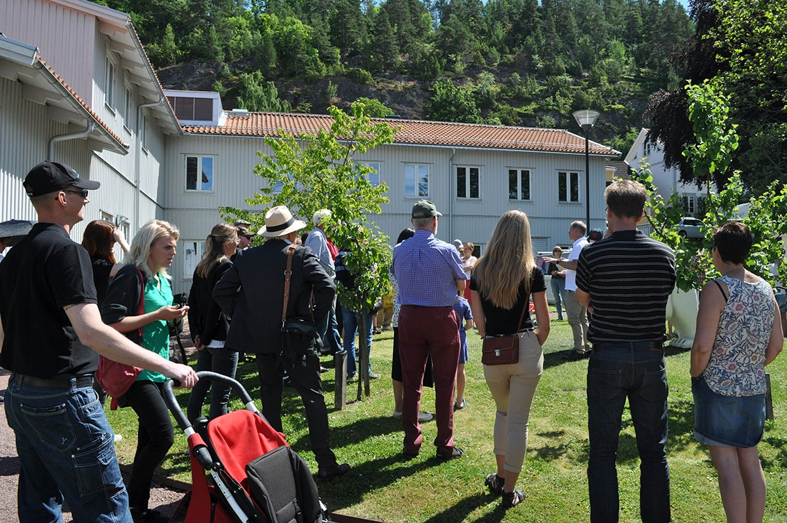 Folksamling på gården till Grenna Museum. En man i vit pikétröja håller ett tal. Folk runtomkring.