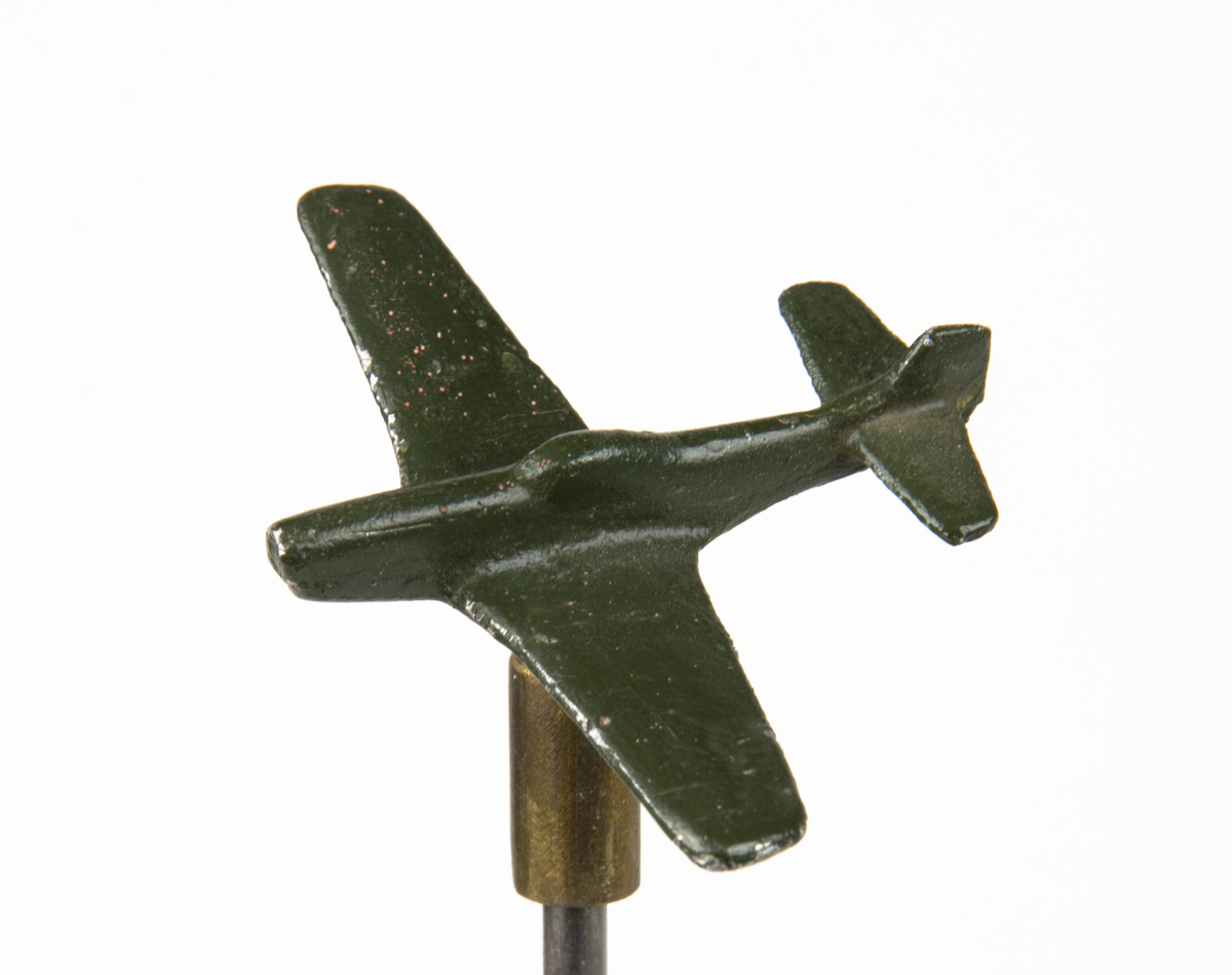 Flygplansmodell, J 26, North American P-51 Mustang. Gjuten modell av metall monterad på en höj- och sänkbar pinne med en tyngd nedtill och ett ledat fäste för flygplanet.