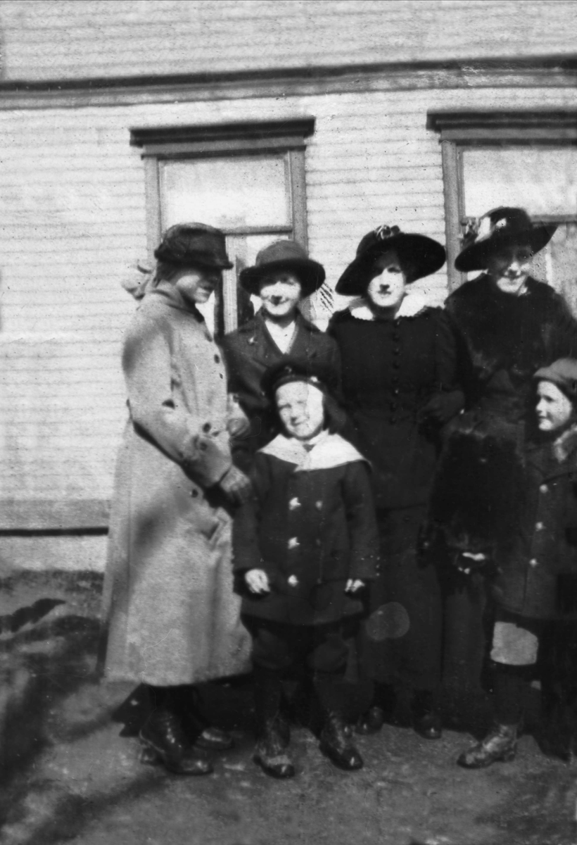 Fire kvinner og to barn stående foran en bygning.