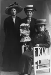 Studioportrett av tre kvinner, en av dem holder en dukke.