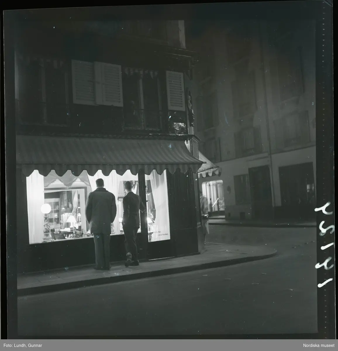 1950. Frankrike. Kvällsbild, två män framför skyltfönster