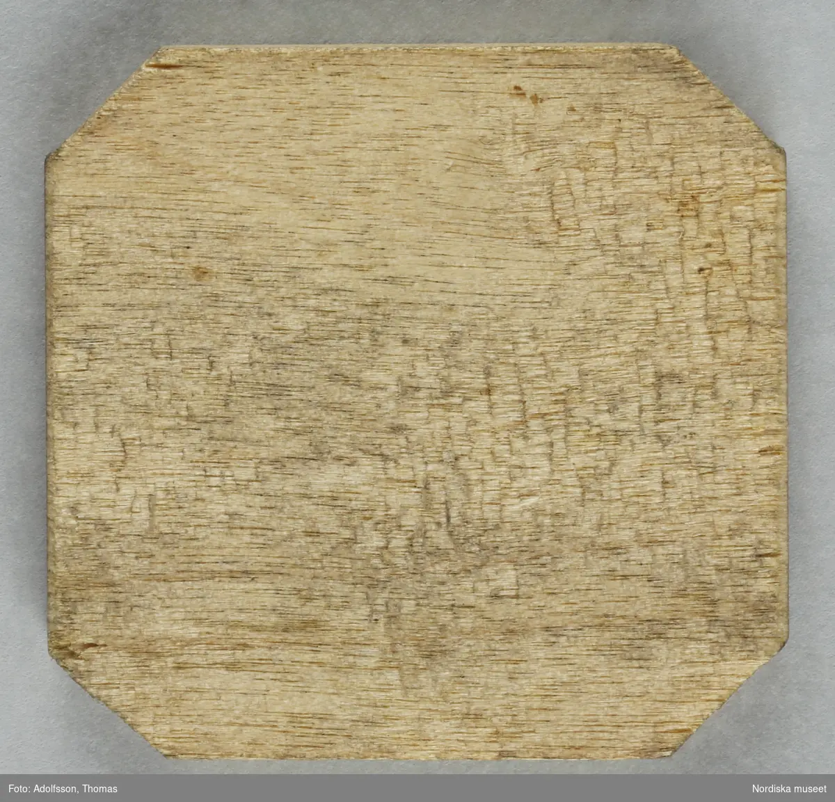 Fyrkantig pollett av trä, med avklippta hörn. Stämplad: 2