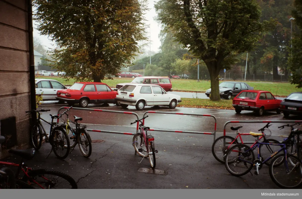 Parkerade cyklar och bilar utanför en stenbyggnad. Mölndalsbro i dag - ett skolpedagogiskt dokumentationsprojekt på Mölndals museum under oktober 1996. 1996_1190-1211 är gjorda av högstadieelever från Kvarnbyskolan 9D, grupp 4. Se även 1996_0913-0940.