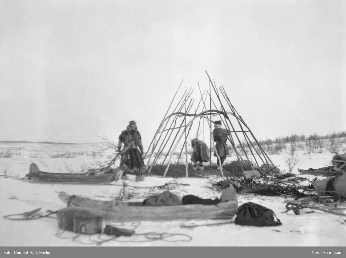 Tre personer, Gate och Heikka/ Jouna och Anne Rasti samt deras dotter Rauna/ Marge, har slagit läger och reser en kåta i Tromsdalen under vårflyttningen från Närvä. Bilden ingår i en serie fotografier tagna av Emilie Demant Hatt i Sapmi mellan åren 1907 och 1916.
