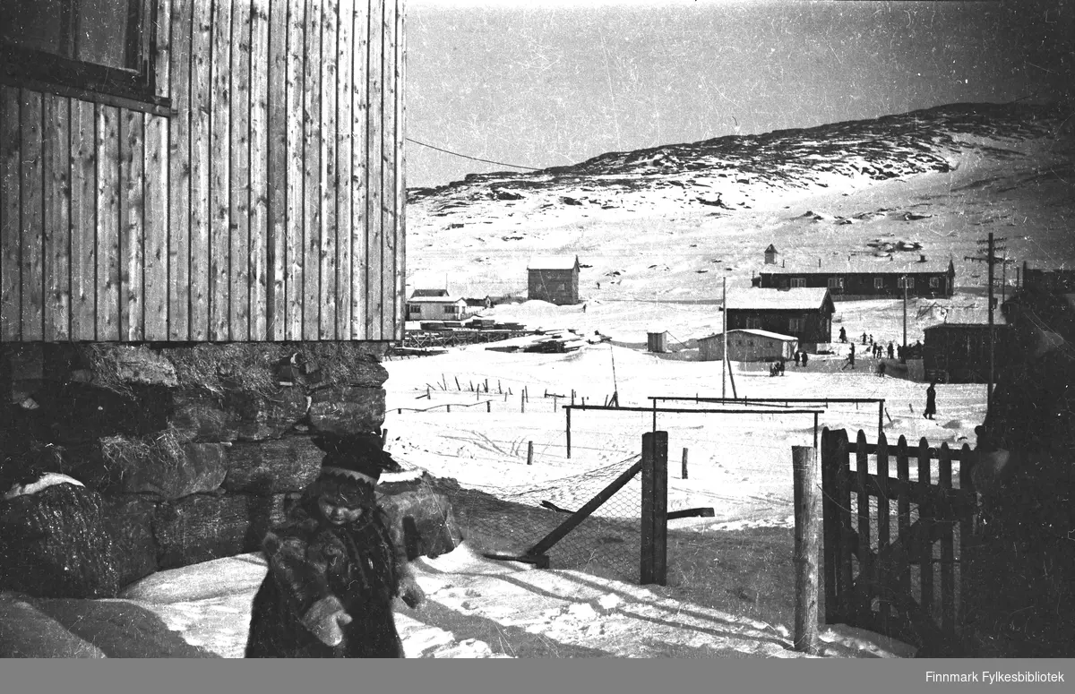 Havøysund 1949. Et lite barn i forgrunnen har samisk barnepesk og samisk lue på seg. Kirkebrakka i bakgrunnen.
