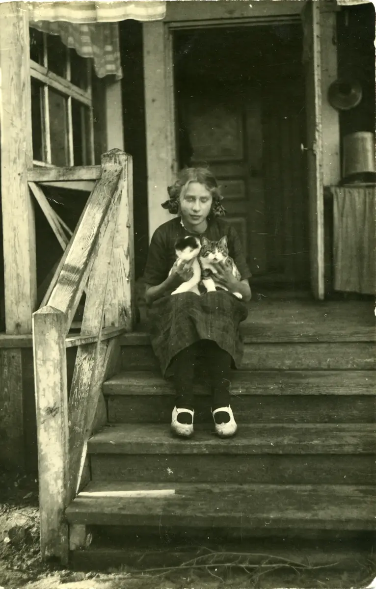 Märta Lindgren f. Olsson, Rådalen, sitter på trappan med två katter i famnen. Ca 13 år.