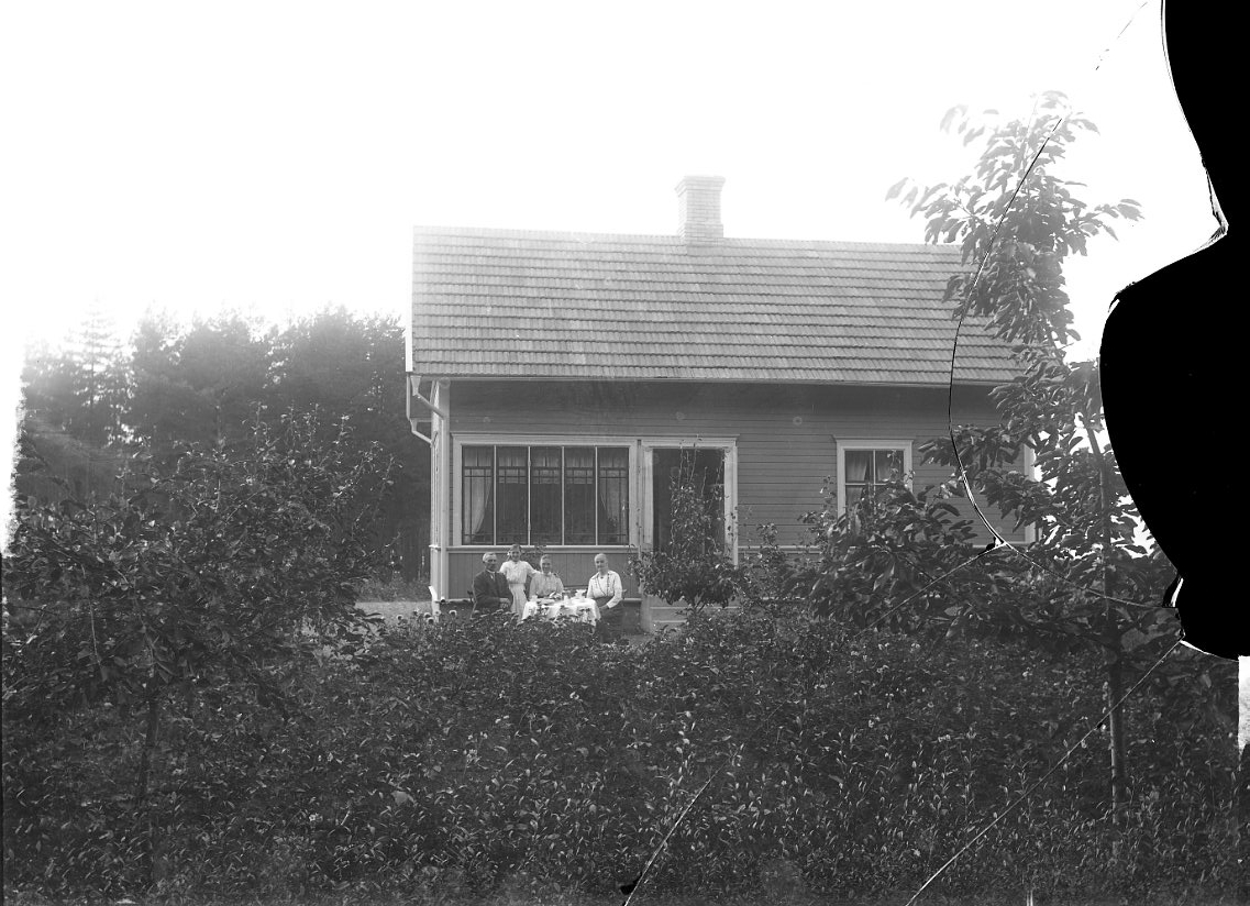 Tre vuxna och ett barn vid ett dukat kaffebord framför ett bostadshus.