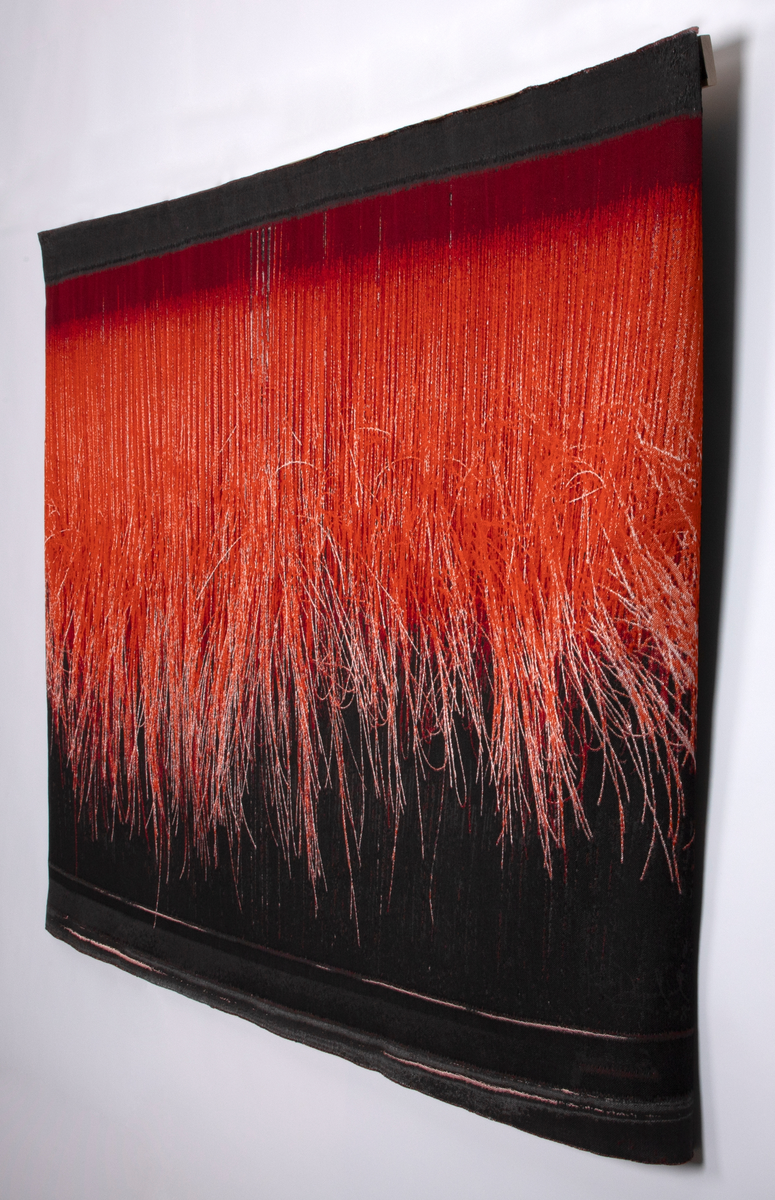 Digitalt vevd veggteppe med ulike nyanser av rødt, flankert av mørk grå (gråbrun). Teppet viser veven slik den ser ut for den som vever, når vedkommende ser ned, ifølge kunstneren. Et rødt teppe som blir vevd, med de løse trådene hengende ned, mot en mørk bakgrunn.