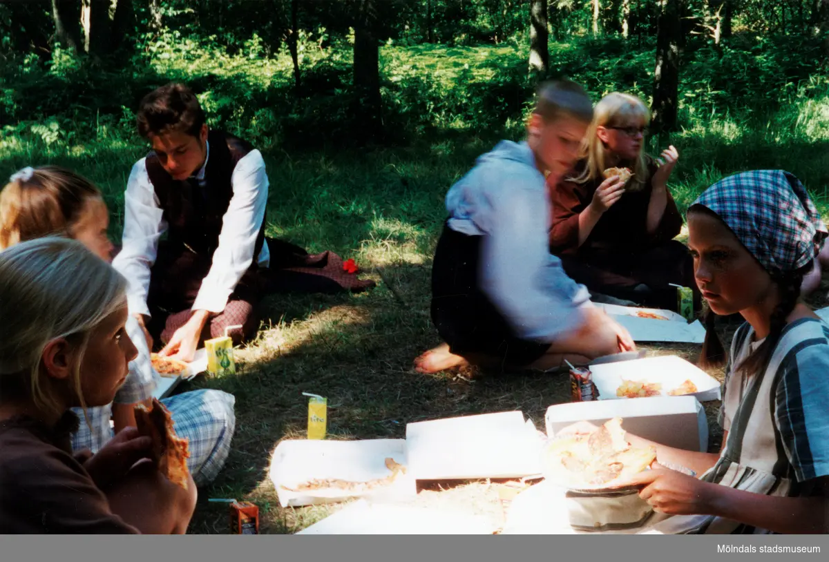 Sommarspelet/barnteaterföreställningen "Rasmus på luffen" 1999 vid Byxorna i Gunneboskogen (korsningen Christina Halls väg/John Halls väg). Barn som ska delta i föreställningen sitter och äter pizza i naturen.
