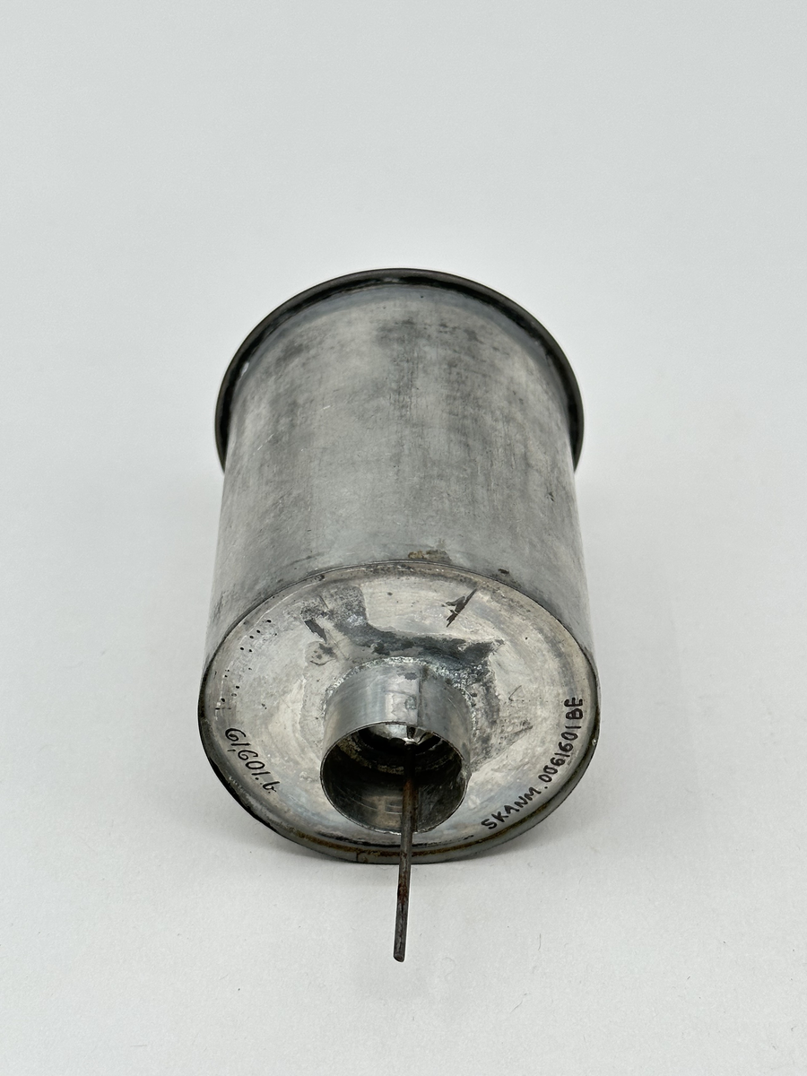 Oljehus, till rovoljelampa. Cylinderformat, av vitmetall. I toppen ett fäst mässingslock med knopp, i botten en pipa med utstickande flottör. 