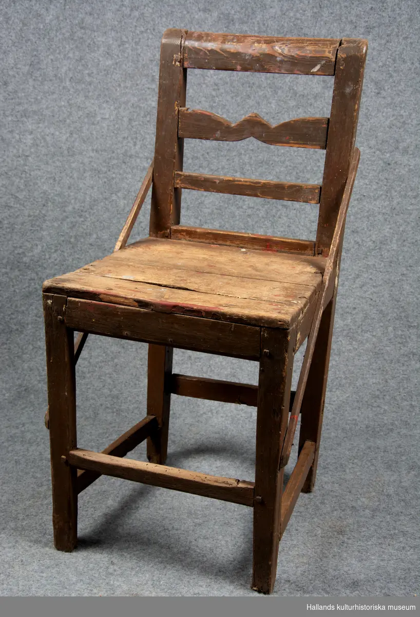 Stol i brunmålat trä. Två trälister går på var sin sida om stolen diagonalt från ryggstödet ner till de främre stolsbenen.