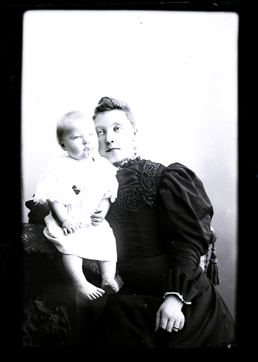Atelierfoto. En kvinne og et småbarn.
Skrevet på papir som er festet til negativet: 260  Klara Skarkerud, se bilde GM_MG.01296_1.