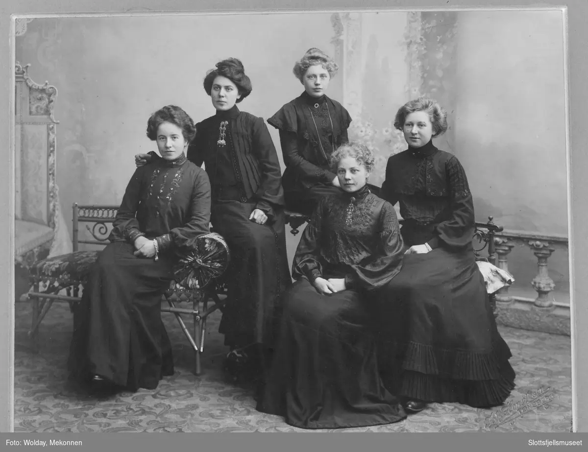 Fem sittende kvinner i mørke kjoler.