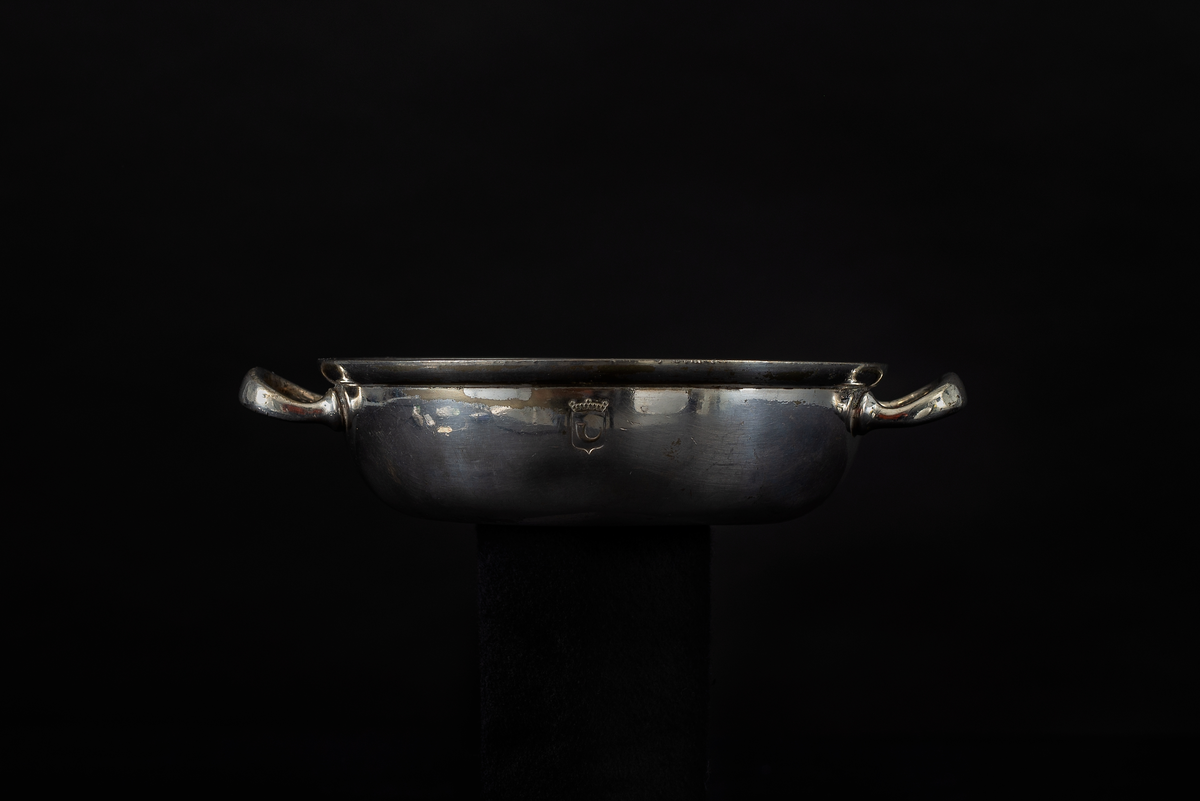 En serveringsskål, med handtag. På sidan ett ingraverat vapen, ett krönt posthorn. Skålen har troligen använts på jagaren Klas Horn.