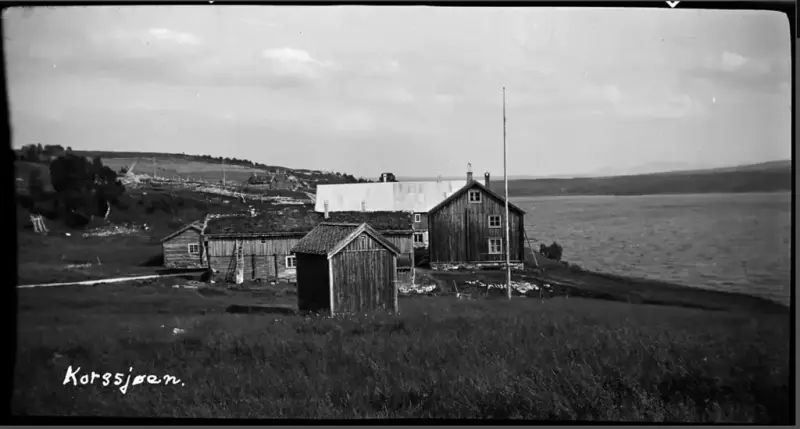 Gammelt bilde i svart/hvitt. Gammel gård med jorde fremst i bilde, og sjøen og flere jorder i bakgrunnen. Bildet er tatt på en sommerdag med pent vær.