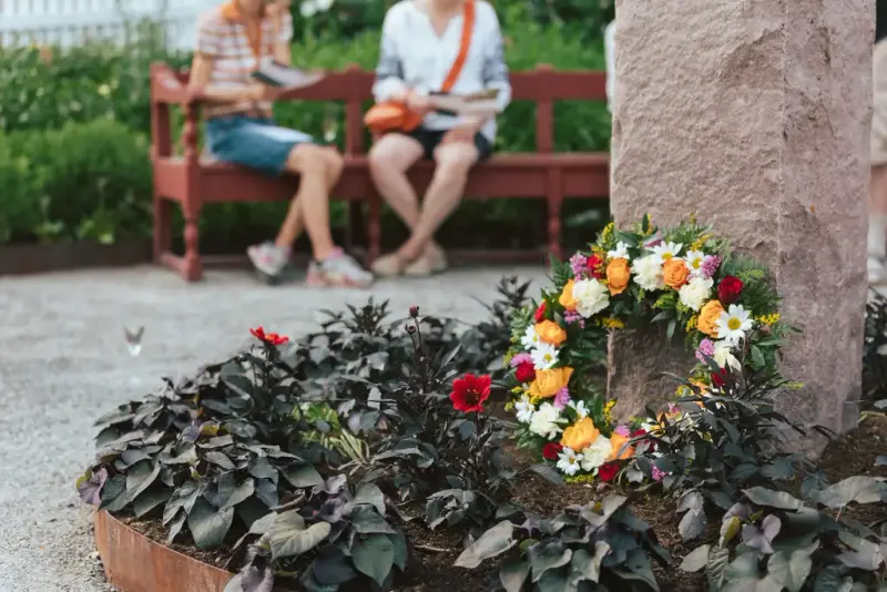 Fotografi av blomsterbedet ved bysten av Kirsten Flagstad museum. Foran bysten ligger en fargerik blomsterkrans