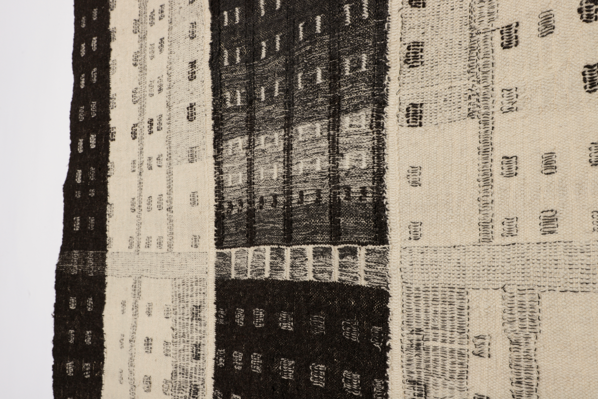 Veggteppe vevd i svart og hvit ull, renning av lin. Fargene fremtrer som nyanser i grått, hvitt og svart. Motivet er inspirert av Manhattans skyskrapere med fremtredende vertikallinjer mønstret av bygningenes vindusrekker. Den nedre del er horisontalbetont med Brooklyn Bridge som inspirerende motiv, tildels med sikksakk-linjer. Frynser nederst.
