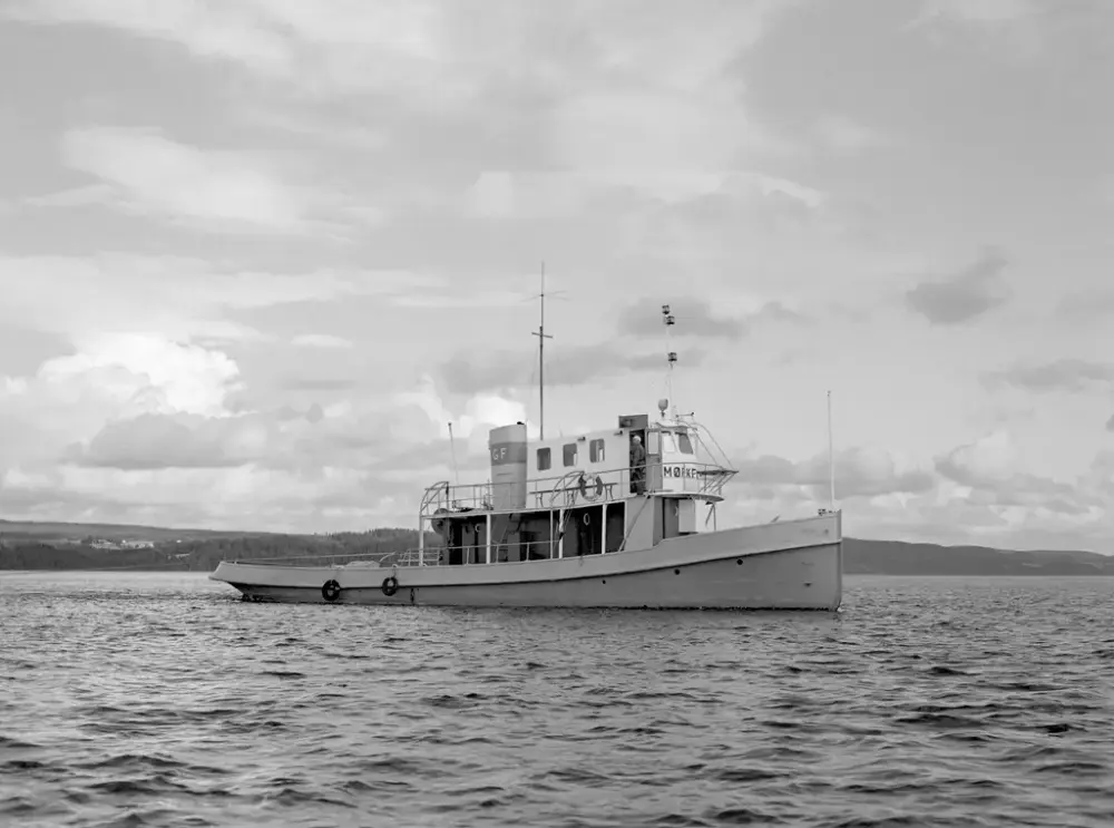 Sort-hvitt fotografi av slepebåten MB Mørkfos som kjører ute på rolig vann.