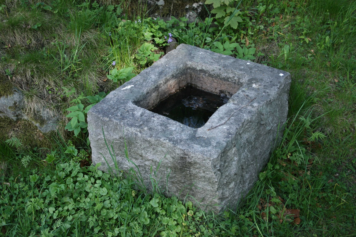 Rektangulær  steinblokk med et rektangulært forsenket vannkarl på toppen, ca. 15 cm  dypt. En smal avløpsrenne midt på den ene langsides karm.  Grovt  tilhugget overflate. 

