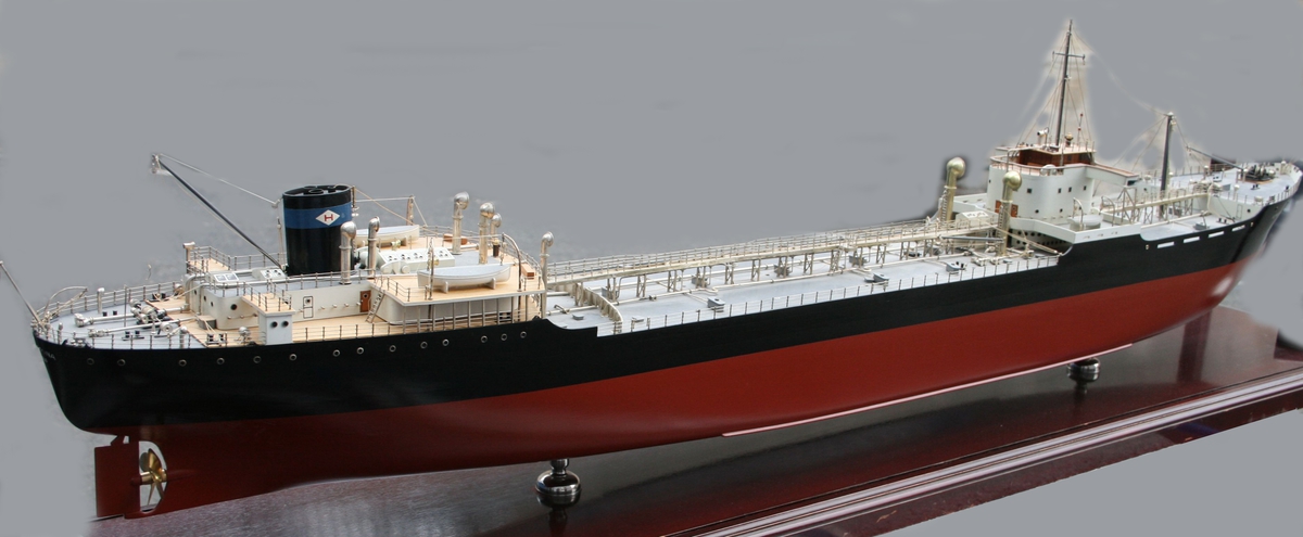 Skipsmodell, tankbåt, i monter. Pipemerke: Blått bånd rundt sort pipe, hvit rombeformet felt med rød bokstad H.  Monteren er beiset i palisanderfarge og lakkert.