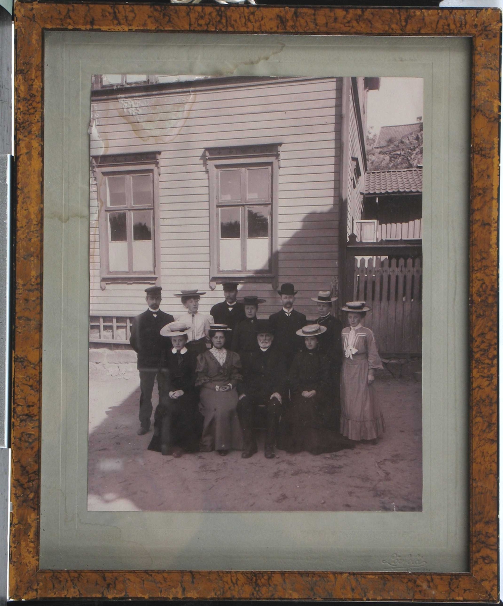 Fotografi tatt utendørs foran skolebygning, av en gruppe lærere, 4 menn og 7 kvinner. Kvinnene er ikledd fantastiske hatter. 
