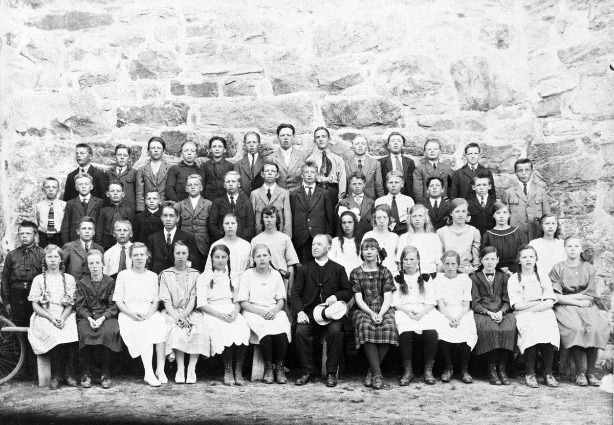 Konfirmanter ved Skedsmo kirke 1922
Konfirmantene oppstilt mot kirkemuren. Sogneprest Larsen i sivil, sittende midt i flokken